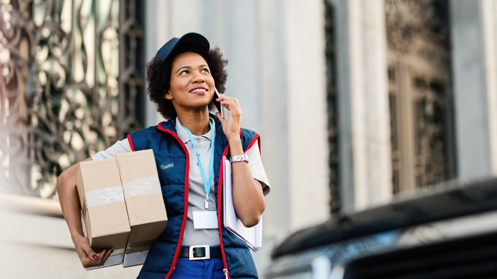 Courrier du dernier kilomètre CIRRO Parcel à Paris tenant des colis et parlant au téléphone, présentant des solutions de livraison flexibles comme le transport multimodal et la communication améliorée avec les clients pour les Jeux Olympiques 2024.